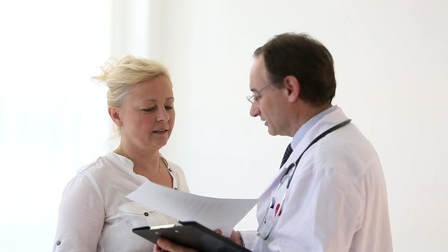 Worried blonde woman receiving prescriptions from her doctor, showing her papers results on clipboard