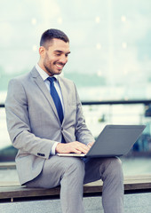 smiling businessman working with laptop outdoors