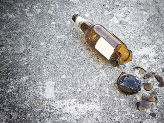 Shattered brown beer bottle resting on the ground: alcoholism concept
