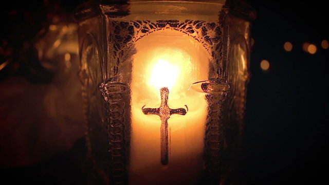 Single candle in thick glass container baring cross