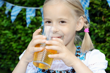 Kind im bayrischen Biergarten trägt Dirndl als Tracht und trinkt Apfelsaft