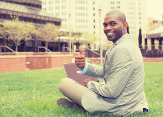 smiling businessman working with laptop outdoors giving thumbs up