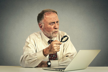 senior man working looking through magnifying glass at laptop screen