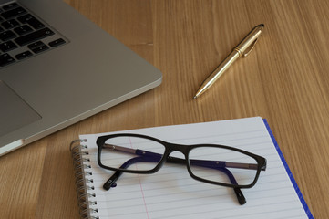 Glasses, note book, pen, and computer on an office desk