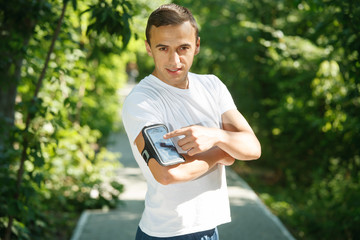 Fototapeta premium Male athlete running in the park while getting ready for workout,healthy fit runner setting her personal trainer application or stopwatch on cell phone before a run