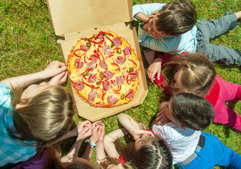 Happy children eating pizza outdoors