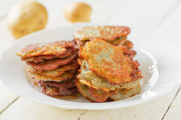 potato fritters/ hash browns with a golden crust in a white ceramic plate and crude potatoes on a...