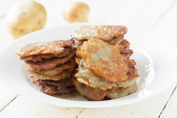 hash browns/ hash browns with a golden crust in a white ceramic plate and crude potatoes on a table