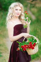 Beautiful young blonde woman with curly hair holding a basket full of red roses. Soft focus