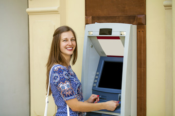 Fototapeta na wymiar Young woman in summer dress using an automated teller machine