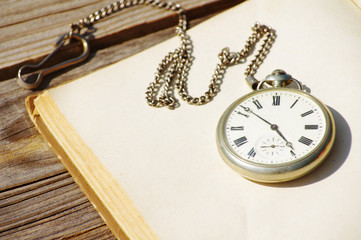Old pocket watch and the open book with blank empty pages on a linen cloth