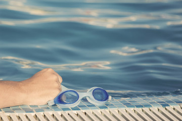 Hand holding goggles at the pool edge