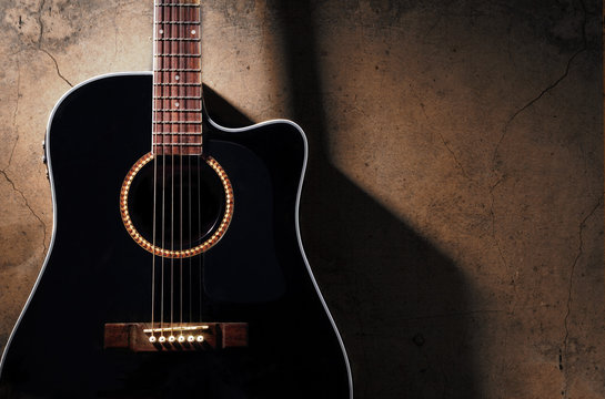 Black acoustic guitar on the old dirty wall, with shadow