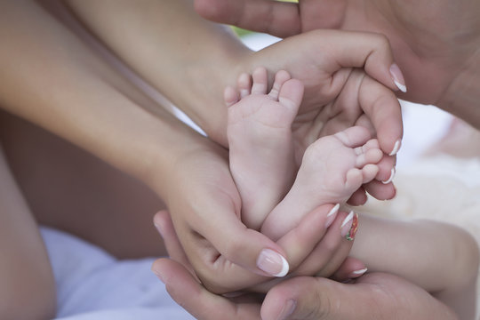 Happy family of parents holding bare feet with small toys and soft skin of little tiny baby with male and female hands outdoor closeup, hotizontal picture