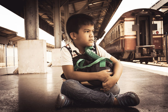 vintage tone, boyl sitting alone with suitcase at Railway Platfo