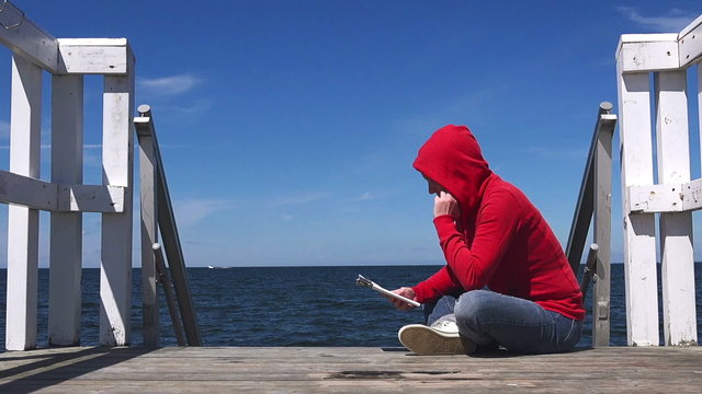 Alone Young Woman Reading and Sitting at the Edge of Wooden Pier Looking at Water.