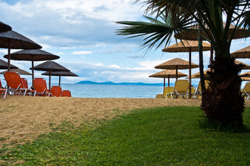 Entrance to sandy beach with stray sunshades and orange chairs