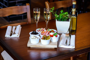 Italian aperitif from a variety of snacks on a table for date/Appetizers of vegetables, pickles, cheese and meat on a table with glasses of champagne