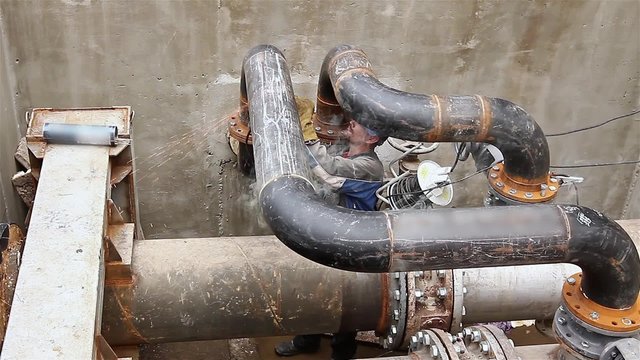 Manhole, metalworker is preparing pipeline node for welding. Metal worker is grinding weld on pipe junction in a manhole for pipeline system.