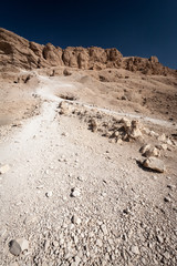 Valley of the Kings path and tombs. A view along a narrow path leading up the limestone cliffs towards openings in the cliffs which identify tomb entrances.