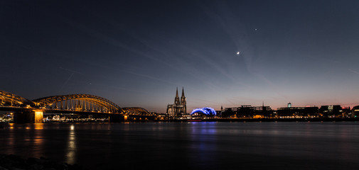 Fototapeta na wymiar Köln mit Dom (beleuchtet) über den Rhein. Mit Deutzer Brücke und Sichelmond