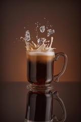 Ice cappuccino splash, refreshing mug of coffee on brown background.