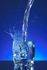 Water poured into a glass, splash, blue background, refreshing, freshness and health. Water bottle, water pitcher, blue liquid, ice, drops, motion, wave, splash, transparent blue water,
