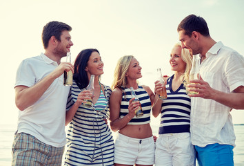 smiling friends with drinks in bottles on beach