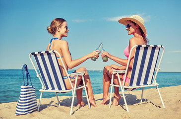 happy women clinking bottles and drinking on beach