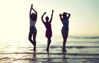 happy female friends dancing on beach