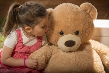 Portrait of expressive little girl kissing her toy bear