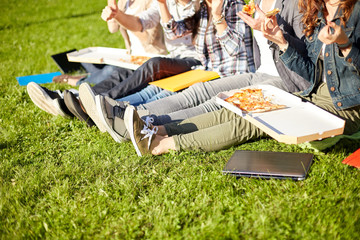 close up of teenage students eating pizza on grass