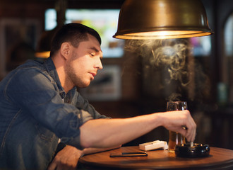 man drinking beer and smoking cigarette at bar
