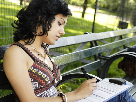 A Beautiful Young Woman Seated On A Park Bench Filling Out A Job Application.