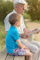 Senior man and child reading a newspaper outdoors
