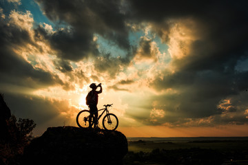 Naklejka na ściany i meble Silhouette of a biker and bicycle on sky background.