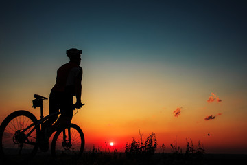 Obraz premium Silhouette of a biker and bicycle on sky background.