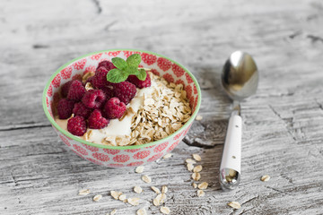 oatmeal with raspberries and natural yoghurt in a bowl on a light wooden background