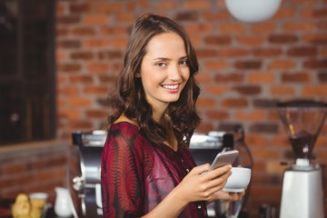 Pretty woman holding a cup of coffee and texting