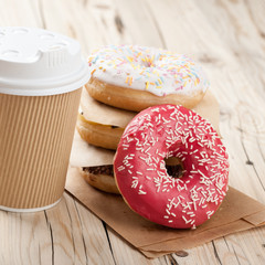 Colorful donuts and paper cup on wooden table