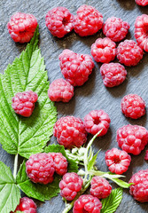Juicy ripe raspberries with leaves on a dark stone background, t