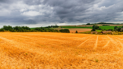Fototapeta premium Bauernhöfe unter bewölkten Himmel und geerntete Getreidefelder
