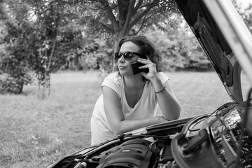 Young attractive girl with a broken car. Young girl with sunglasses, leaning on the car that broke down. She is calling for road assistance. 

