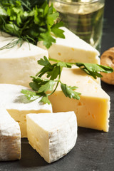 Assorted different kinds of cheese, nuts, herbs, white wine on a