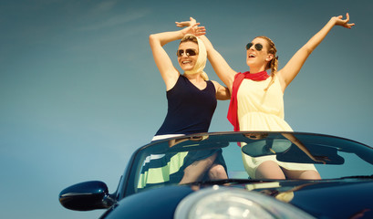 Zwei Frauen in Cabrio genießen einen Auto Ausflug im Sommer und strecken die Arme aus