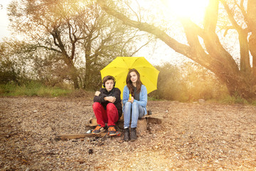two teenager with umbrella sitting on a dirty beach with sun in