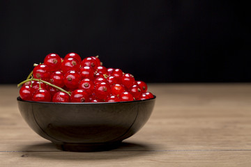black bowl with redcurrants on a wood table, black background