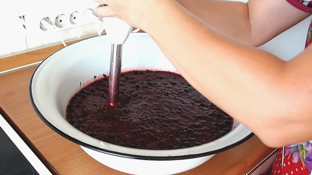 Woman makes blackcurrant jam in a large bowl 