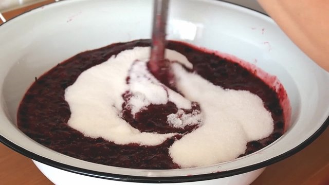 Woman blending jam with blackcurrants and sugar in a large bowl