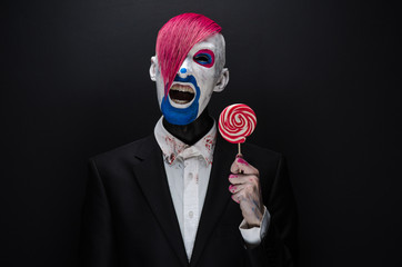 Clown and Halloween theme: Scary clown with pink hair in a black jacket with candy in hand on a...